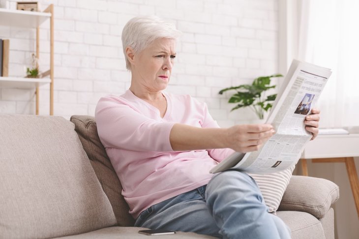 Ældre kvinde der har svært ved at læse sin avis på grund af dårligt syn